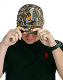 Model wearing camo performance hat with orange X by Nightclubssuck